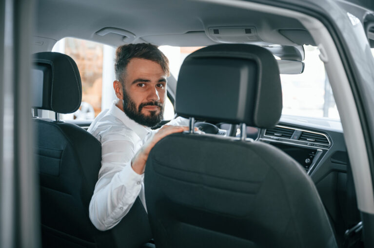 Looking behind. Young man in white clothes is in the car dealership.